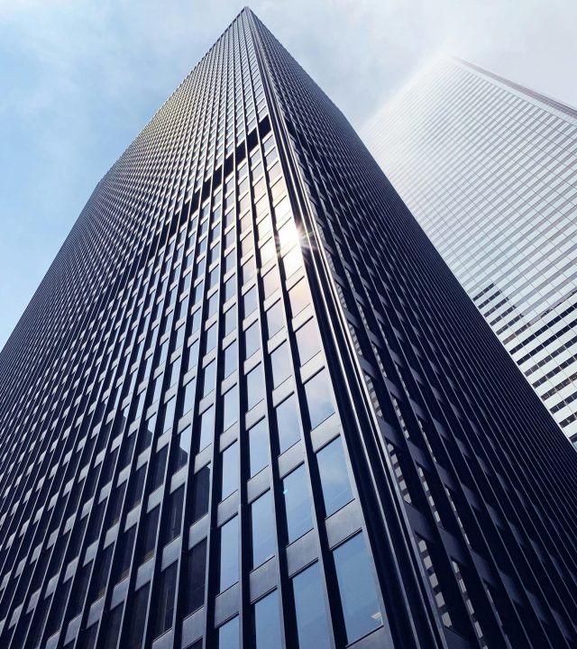 Low angle view of a sleek skyscraper with glass facade in downtown Toronto, capturing sun glare.